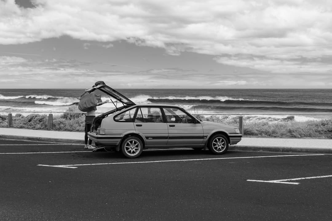 A white rental sedan parked at an Australian coastal lookout, showcasing fuel-efficient travel against a scenic backdrop.