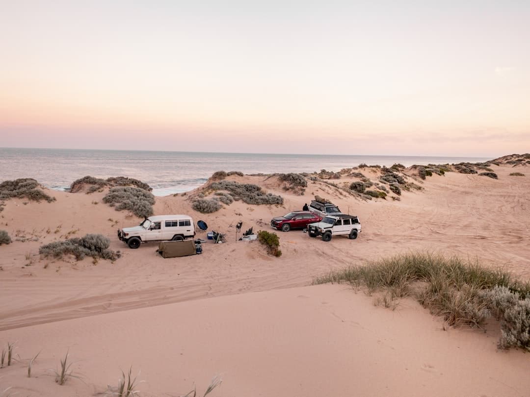 A white SUV parked on a scenic coastal road at sunset, showcasing the beauty of long-term car hire for Australian adventures.