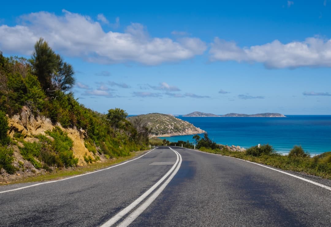 Couple enjoying a scenic coastal view from their white SUV rental car on an Australian road trip.