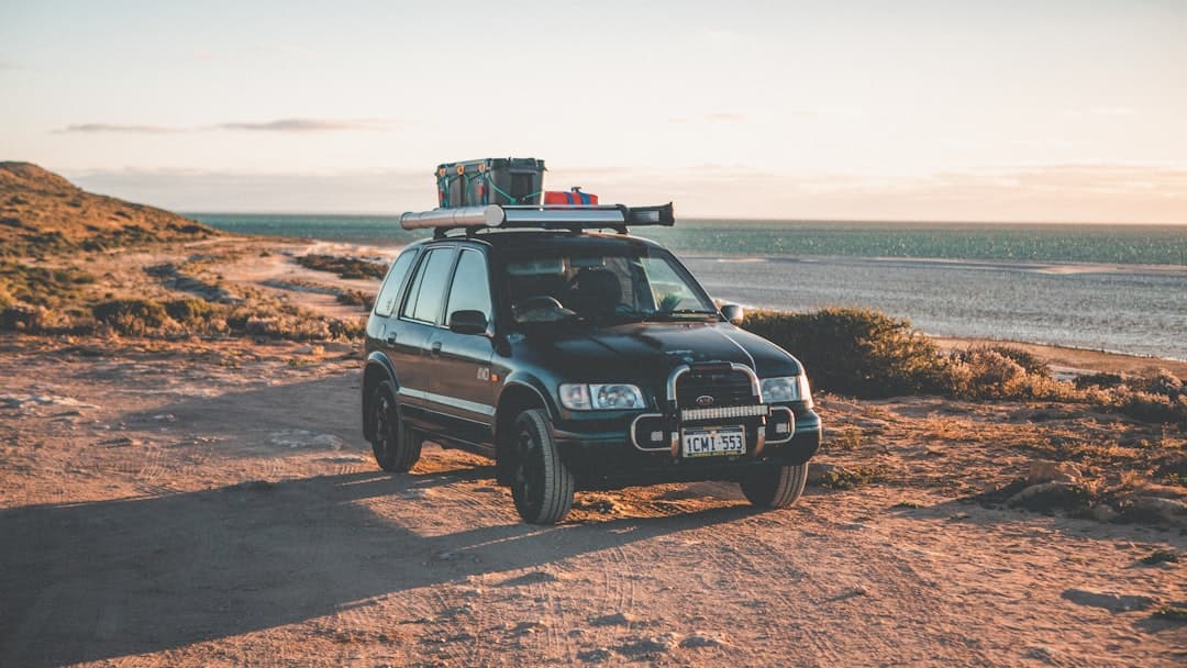 A silver SUV on a dirt track overlooking a stunning Western Australian beach at sunset, ideal for an Australian road trip.